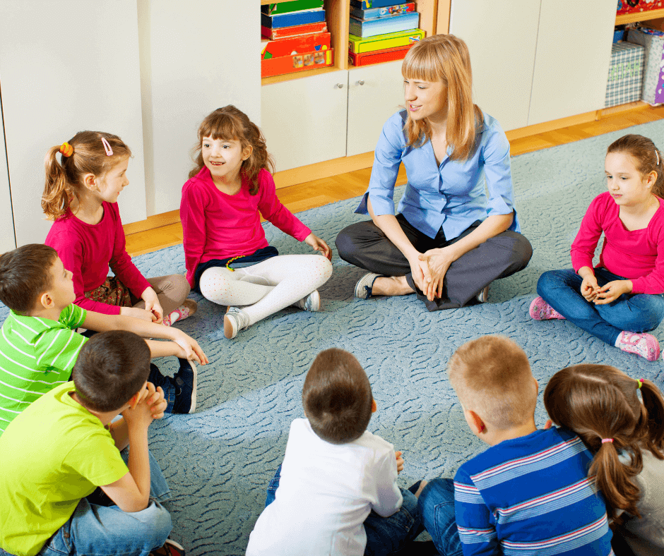 Kids Sitting On Carpet With Teacher And Learning To Pronounce